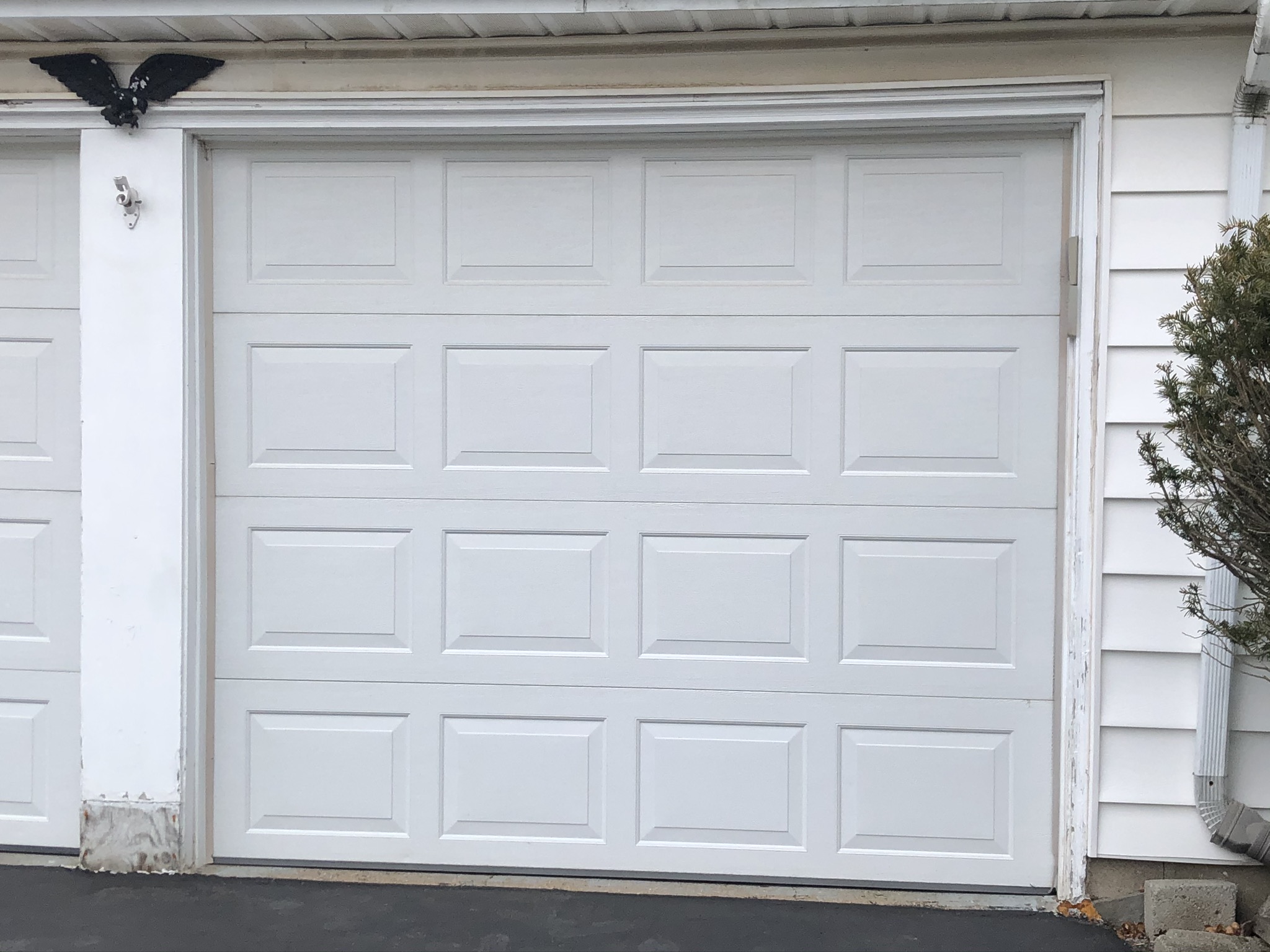 Closed white raised-panel garage door on a white-sided house