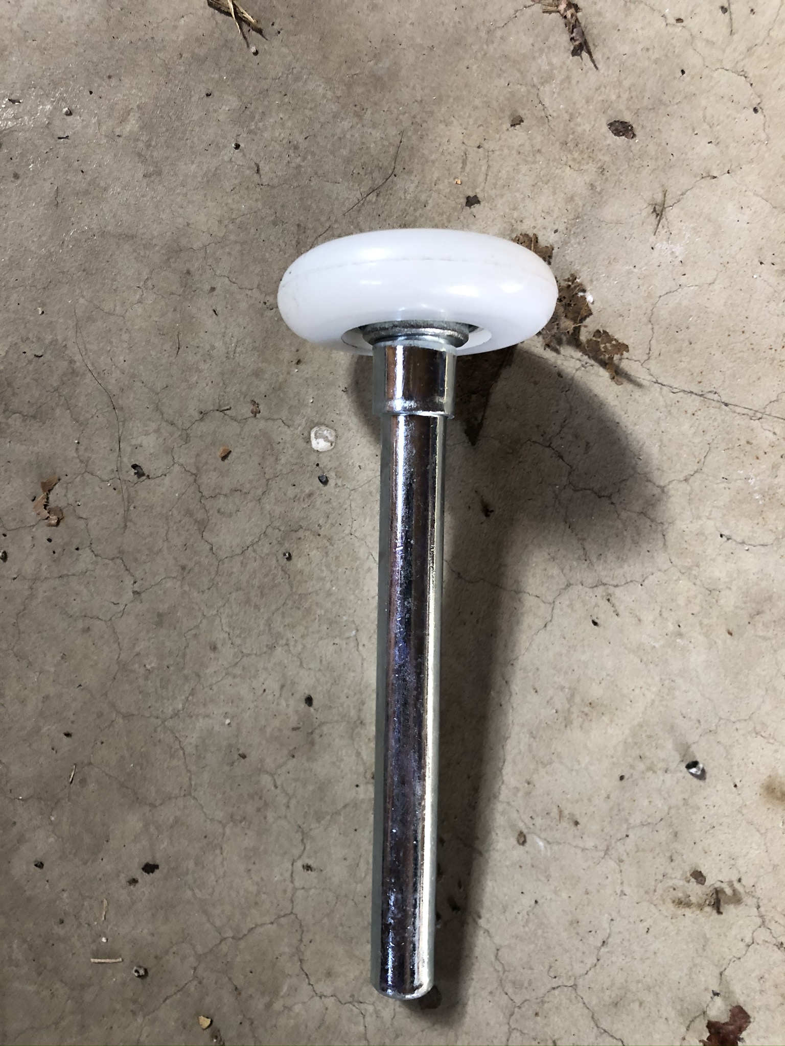 A garage door roller with a white nylon wheel and chrome stem lying on concrete
