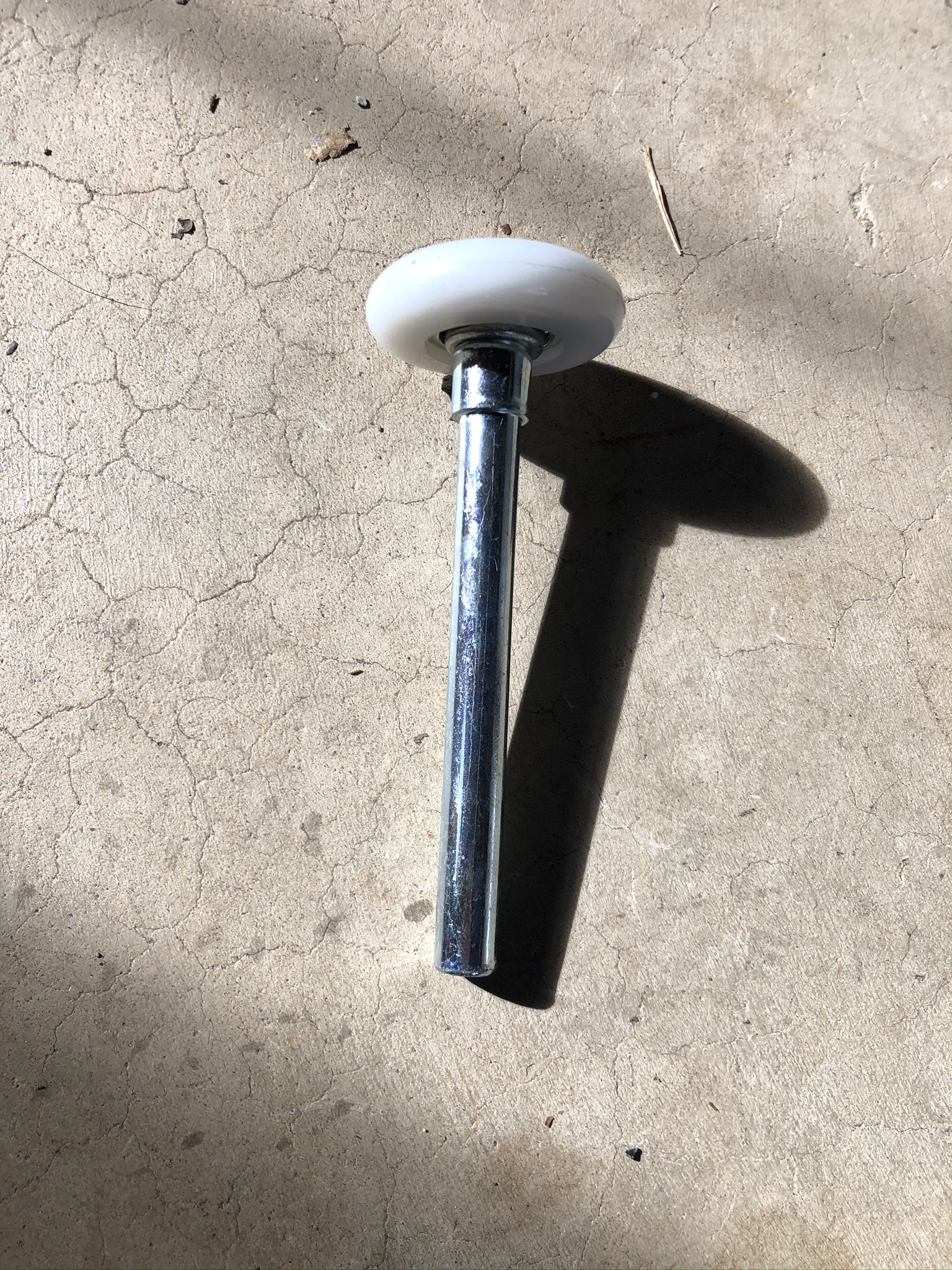 A garage door roller with a white nylon wheel and a zinc-plated steel stem on concrete