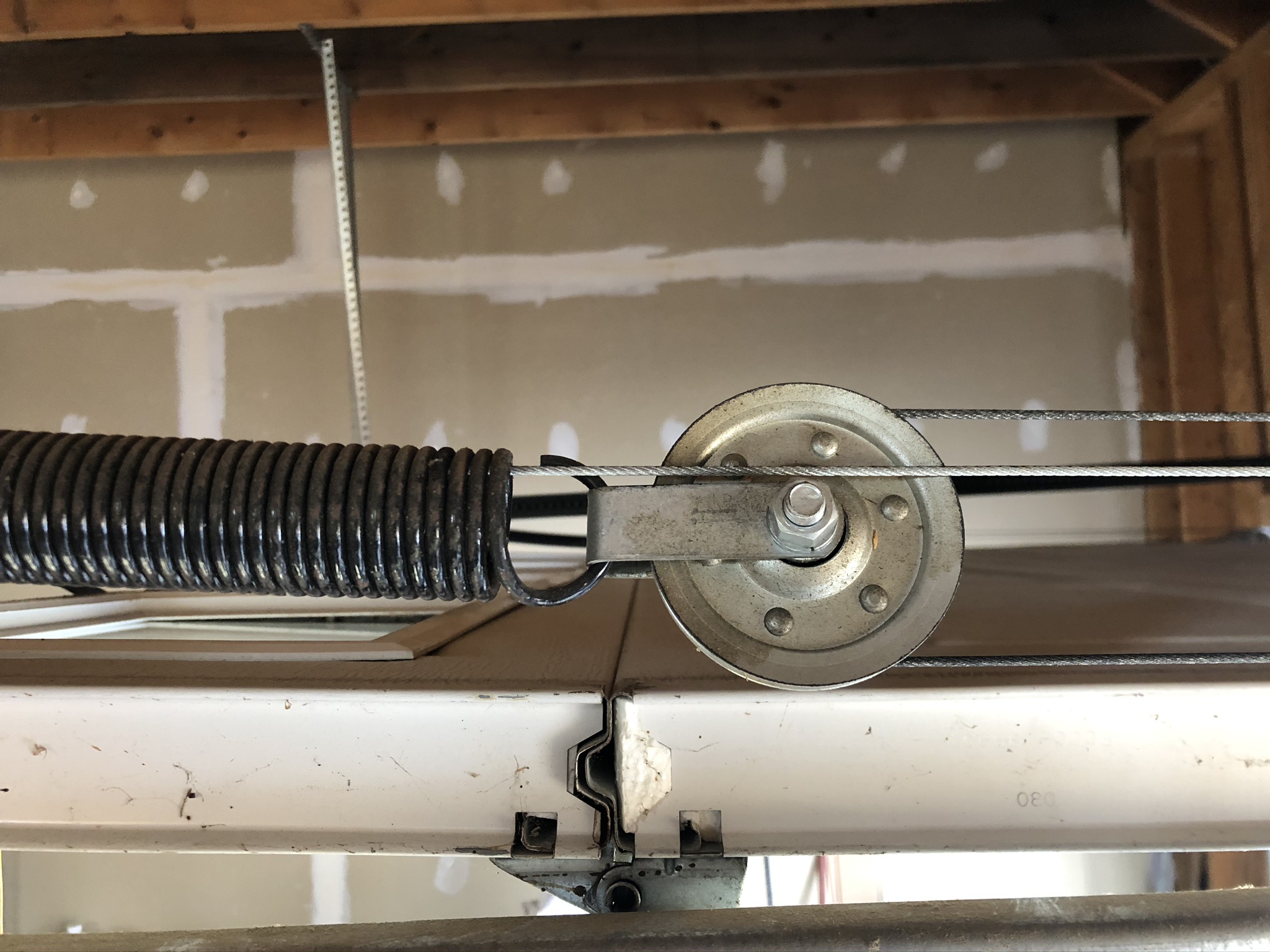 Extension spring, steel cable and pulley above a garage door, close up