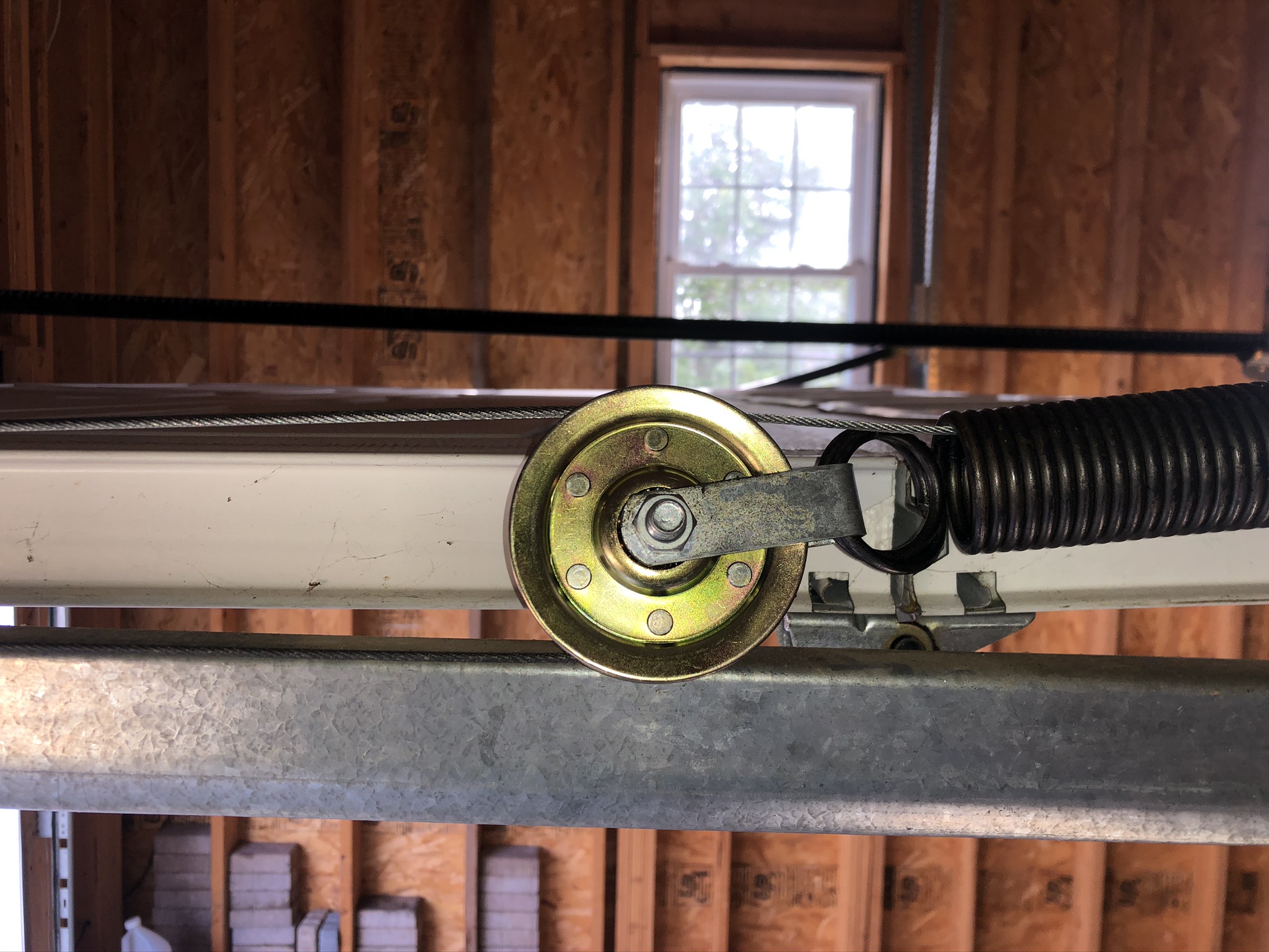 Brass pulley with steel bracket on a galvanized track beside a coiled extension spring